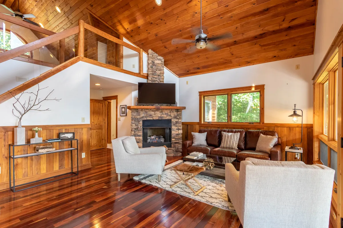 A cozy living area centered around a fireplace, with comfortable seating arranged to enjoy the warmth. Large windows frame sweeping views of the outdoors, bringing in natural light and a sense of connection to the surrounding mountain landscape. The space is inviting for relaxing after a day of outdoor adventure.