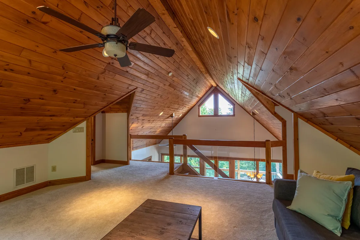 A serene yet spacious lounge with a wooden ceiling, large windows flooding the room with natural light, and a comfortable seating area. The design encourages relaxation or casual socializing, while the windows offer views that connect guests to the outdoors, hinting at nearby nature trails and mountain vistas.
