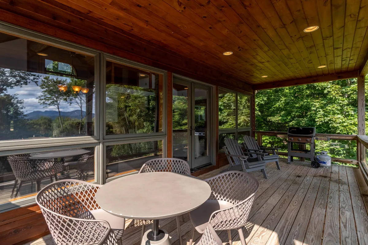 This image highlights an outdoor deck with a table and chairs set up for alfresco dining, a gas grill nearby, and an expansive view of the surrounding mountains in the background. The scene is bathed in natural light, inviting guests to relax, dine, and soak in the scenery.
