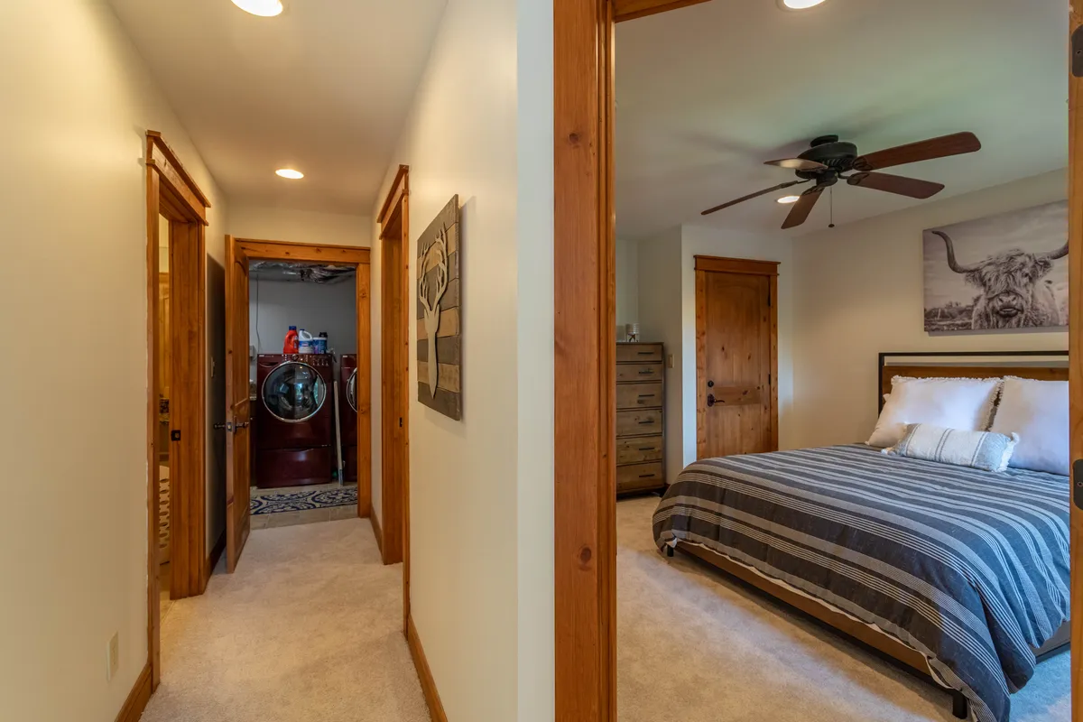 A bedroom with striped bedding is seen in the foreground, while a laundry area is conveniently visible through the hallway. The space feels welcoming and practical, seamlessly integrating rest and household chores.