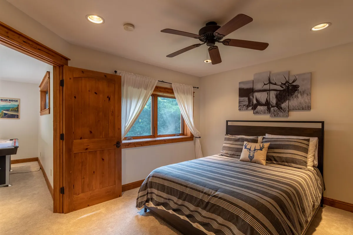 A cozy bedroom featuring a king-sized bed with striped bedding, a window letting in plenty of natural light, and a painting of an elk above the bed. The room exudes a sense of calm and comfort, making it an inviting retreat for relaxation after a long day.