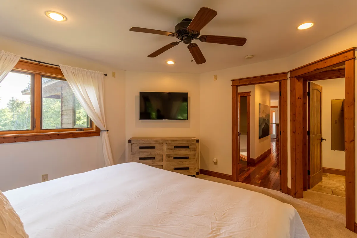 A tranquil bedroom with a plush bed, a window offering mountain views, a TV for downtime, and a dresser. The room is bathed in natural light, creating a soothing atmosphere ideal for recharging after a productive day.