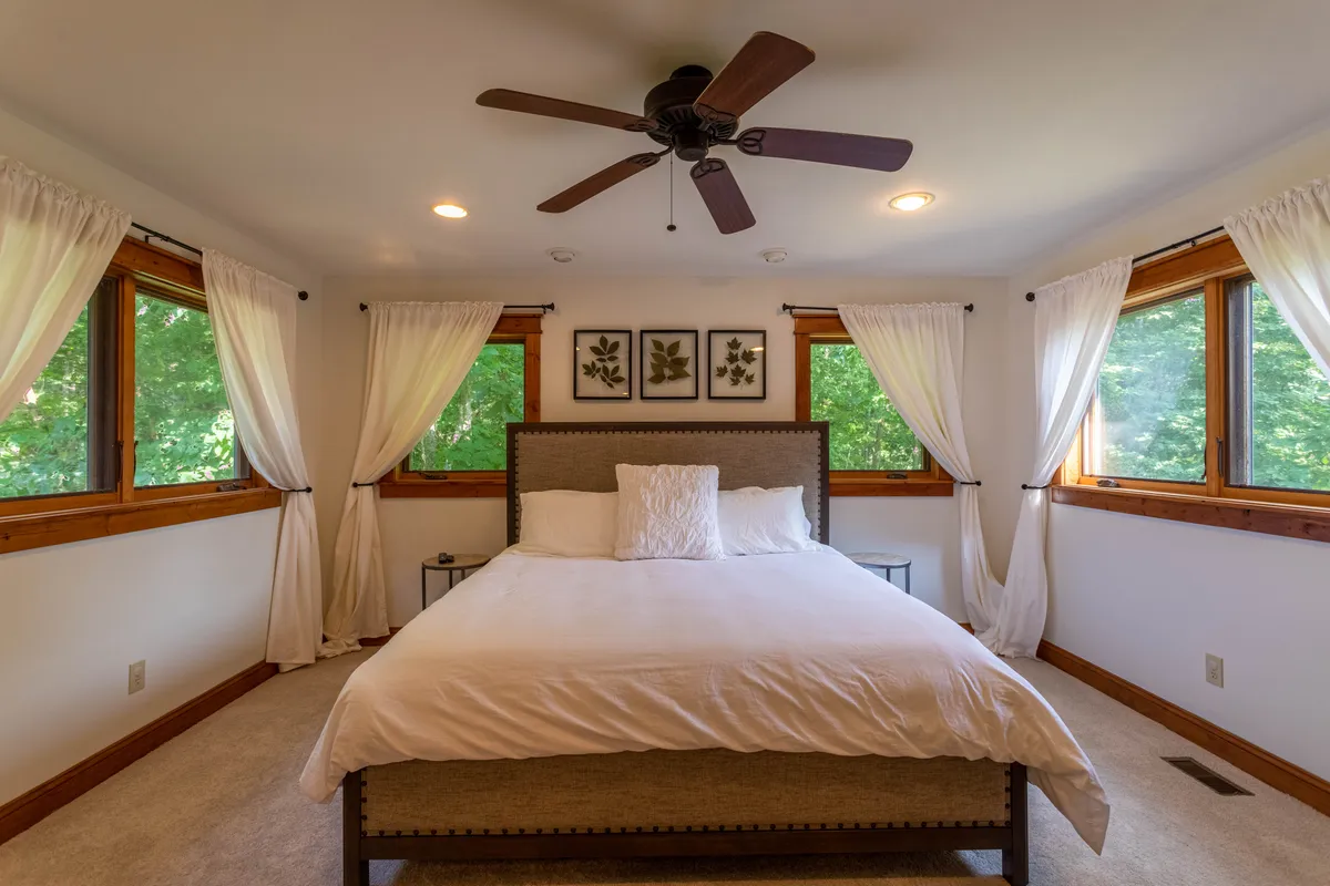 A spacious Queen bedroom with soft bedding, large windows dressed with curtains, and tasteful wall art, creating a peaceful environment for relaxation and privacy.