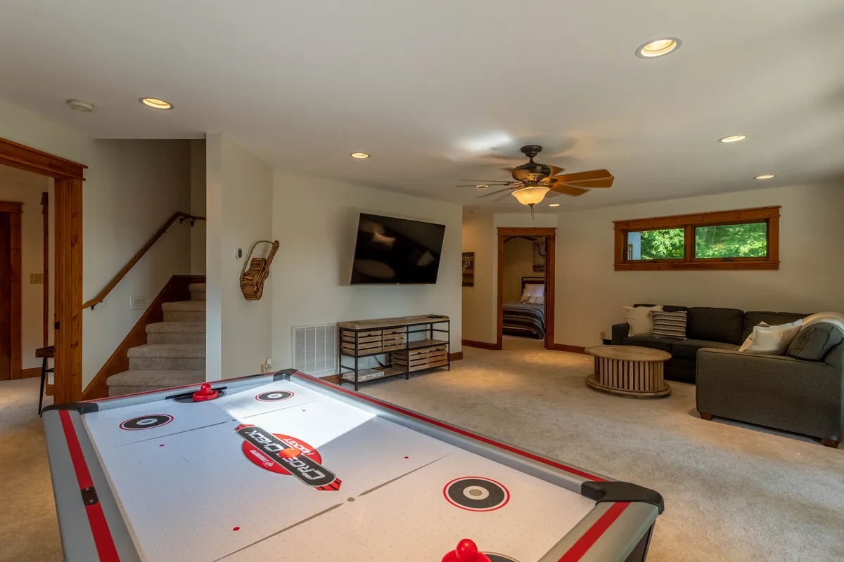 A vibrant game lounge with an air hockey table at the center, a comfortable sofa for group seating, a television mounted on the wall, and a wooden coffee table. The ambiance is casual and fun, inviting guests to play games, watch movies, or simply relax together.