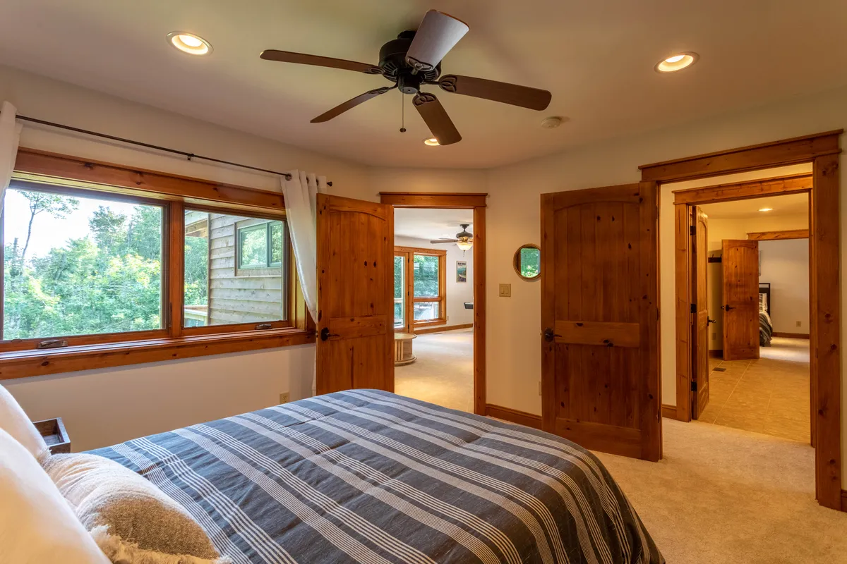 A welcoming bedroom with striped bedding, large windows that fill the room with natural light, and rustic wooden doors and trim. The view outside the windows suggests proximity to nature, making the space feel like a restful retreat after exploring the outdoors.
