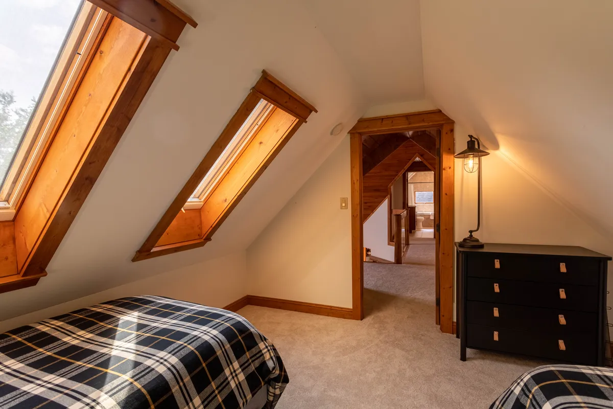 A charming space with twin beds under skylights, black dresser, and exposed wooden beams. The natural light and opportunity to view the sky create a unique, inspiring environment perfect for both quiet reflection and restful sleep.
